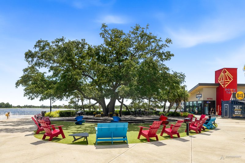 Heritage Tree oak with red Adirondack chairs beside the Grand Lake in Wellen Park
