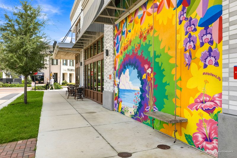 Colorful sun and flower mural marked #WellenLife on a Downtown Wellen building beside the sidewalk